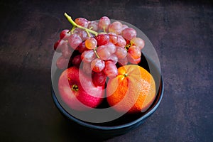 Delicious fresh grapes, orrange and apple on a black bowl.