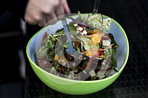 Delicious fresh healthy salad in a green bowl mixed by a woman hands with salad spoon food