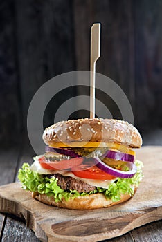 Delicious fresh homemade burger with cheese, tomatoes, salad and onions on a wooden table, close up