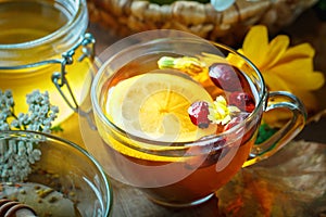 Delicious fresh honey and a Cup of healthy tea with lemon and rose hips on a wooden table. Selective focus.