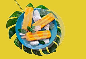 Delicious fresh mango popsicle served with mint leaves and ice cubes isolated on yellow background