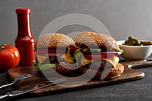 Delicious fresh meat cheeseburgers on wooden board near cutlery, ingredients and ketchup