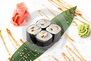 Delicious fresh mini-rolls with cucumber, eel and cheese on a banana leaf. Sushi rolls on a white background with ginger and wasab