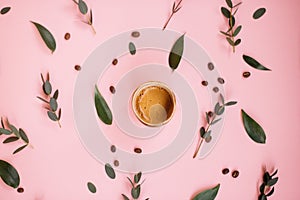 Delicious fresh morning espresso coffee with beautiful crema with eucalyptus leaves and coffee beans on the tender pink background