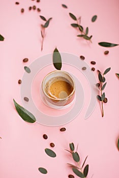 Delicious fresh morning espresso coffee with beautiful crema with eucalyptus leaves and coffee beans on the tender pink background