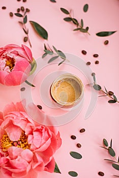 Delicious fresh morning espresso coffee with eucalyptus leaves, coral peony flowers and coffee beans on the tender pink background