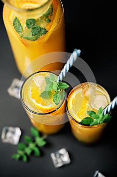 Delicious fresh orange juice with ice, mint and fresh fruits on black table background