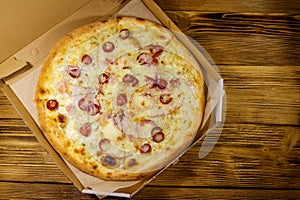 Delicious fresh pizza in cardboard box on a wooden table. Top view