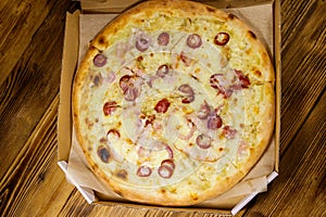 Delicious fresh pizza in cardboard box on wooden table. Top view