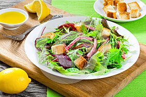 delicious fresh salad of salami and mixed lettuce leaves - baby spinach, arugula, chard in a white dish on the old wooden