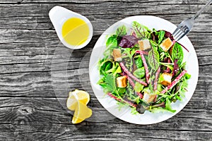 Delicious fresh salad of salami and mixed lettuce leaves - baby spinach, arugula, chard in a white dish on the old wooden table, t