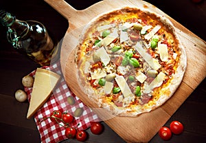 Delicious freshly baked pizza on a wooden paddle topped with tomatoes, parmesan, basil