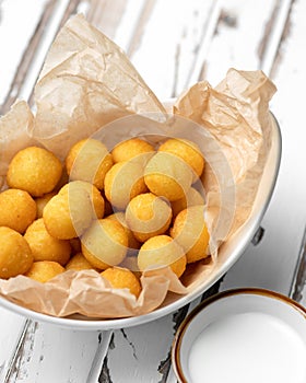 Delicious fried croquette balls in parchment paper. Light snack. Bowl of tasty rustic food on white wooden table