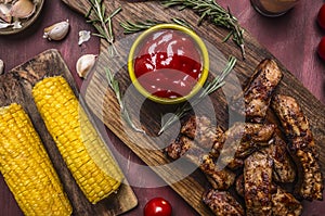 Delicious fried lamb ribs grilled with spicy sauce, herbs and corn on wooden rustic background top view close up