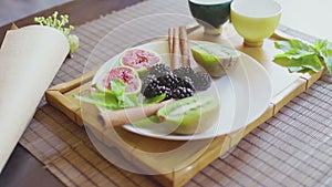 Delicious fruit dish on a plate with fragrant green tea on a wooden tray