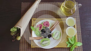 Delicious fruit dish on a plate with fragrant green tea on a wooden tray