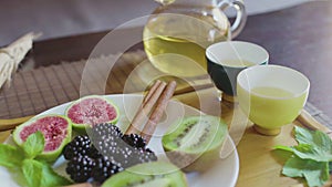 Delicious fruit dish on a plate with fragrant green tea on a wooden tray