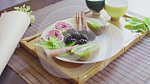 Delicious fruit dish on a plate with fragrant green tea on a wooden tray