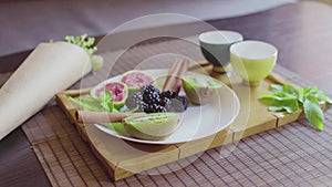 Delicious fruit dish on a plate with fragrant green tea on a wooden tray