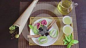 Delicious fruit dish on a plate with fragrant green tea on a wooden tray