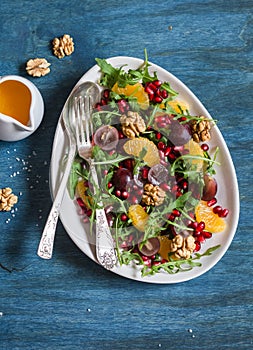 Delicious fruit salad. Grapes, tangerine, pomegranate and arugula fruit salad. On blue wooden background, top view.