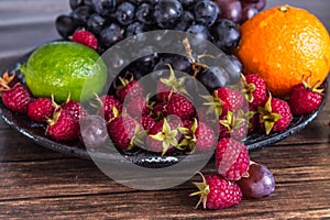 Delicious fruits salad in plate on table, lime, raspberry, grapes
