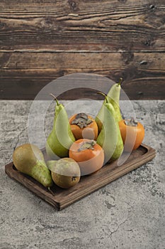 Delicious fuyu persimmons and ripe pears on wooden plate