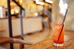 Delicious glass of red lemonade with ice cubes and a straw on a wooden backdrop