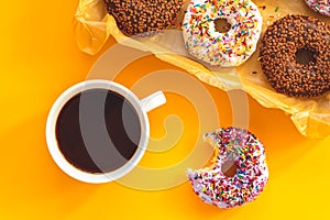Delicious glazed donuts in box and cup of coffee on yellow surface