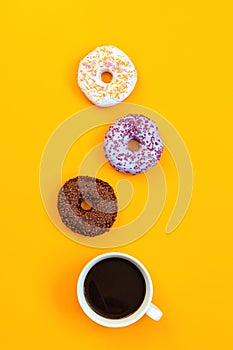 Delicious glazed donuts and cup of coffee on yellow surface