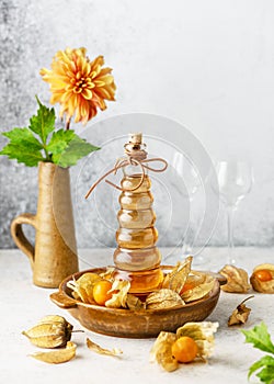 Delicious golden berries liqueur in a glass bottle. Homemade food and drink concept.