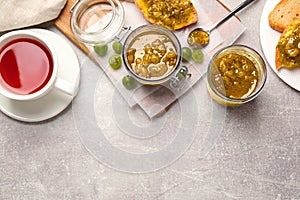 Delicious gooseberry jam, fresh berries and tea on grey table, flat lay. Space for text