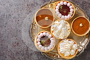 Delicious gourmet sweets tartlets for the holiday with meringue and lemon curd, raspberry curd, nuts and chocolate close-up.