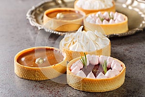 Delicious gourmet sweets tartlets for the holiday with meringue and lemon curd, raspberry curd, nuts and chocolate close-up.