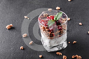 Delicious granola with yogurt and cherry in glass on black background. Healthy breakfast ingredients