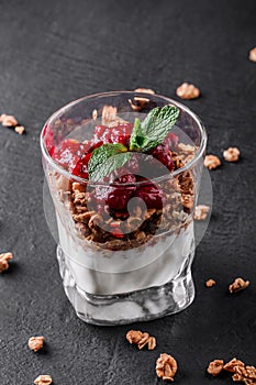 Delicious granola with yogurt and cherry in glass on black background. Healthy breakfast ingredients. Clean eating