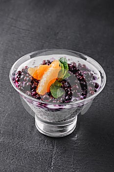 Delicious granola with yogurt, fresh berries, fruits in glass on black background.