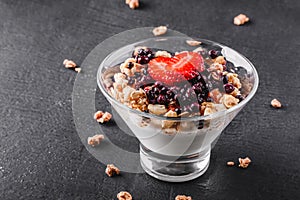Delicious granola with yogurt, fresh berries, strawberry in glass on black background. Healthy breakfast ingredients.