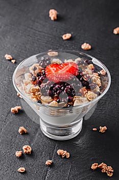Delicious granola with yogurt, fresh berries, strawberry in glass on black background. Healthy breakfast ingredients