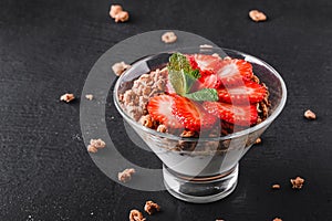 Delicious granola with yogurt and fresh strawberry in glass on black background.