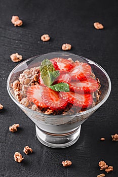 Delicious granola with yogurt and fresh strawberry in glass on black background. Healthy breakfast ingredients