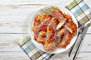 Delicious grated potato coated and deep fried pork chops on a plate on a rustic white wooden table with napkin, fork and knife,