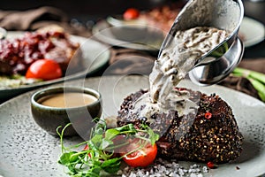 Delicious grilled beef steak with spices on plate with tomatoes and cream sauce over dark background. Concept of bbq food, close