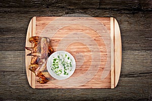 Delicious grilled chicken wings with garlic sauce on a cutting board on wooden rustic background with copyspace top view