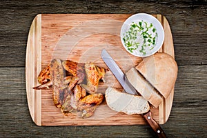 Delicious grilled chicken wings with garlic sauce, knife and bread on a cutting board on wooden rustic background top