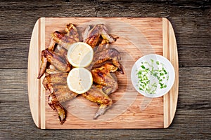 Delicious grilled chicken wings with garlic sauce, lemon on a cutting board on wooden rustic background top view