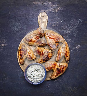 Delicious grilled chicken wings with garlic sauce on a round cutting board wooden rustic background top view