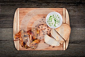 Delicious grilled chicken wings with garlic sauce, spices, seasonings and bread on a cutting board on wooden rustic