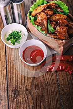 Delicious grilled chicken wings with garlic and tomato sauce with lettuce in food paper bag on wooden rustic background