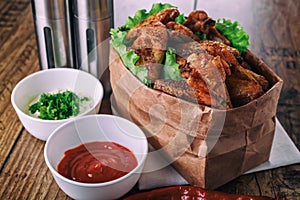 Delicious grilled chicken wings with garlic and tomato sauce with lettuce in food paper bag on wooden rustic background